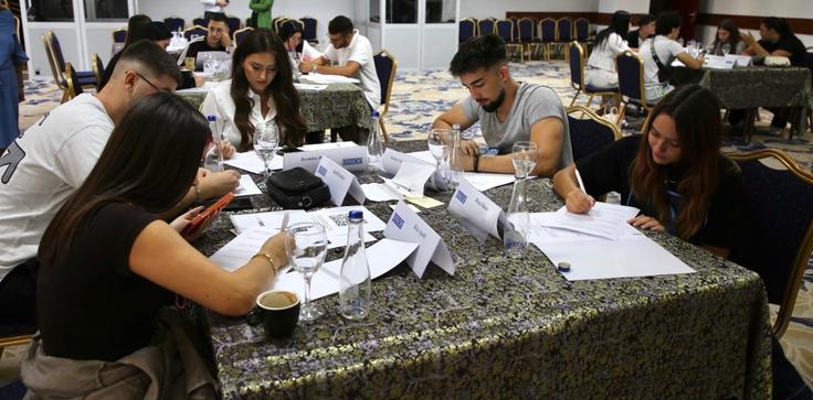 Students sitting at tables in a classroom, concentrating on writing tasks with papers and pens.