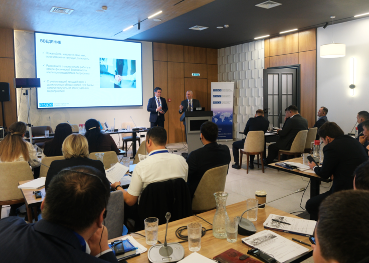People attending a conference in a meeting room with a presentation on a screen.