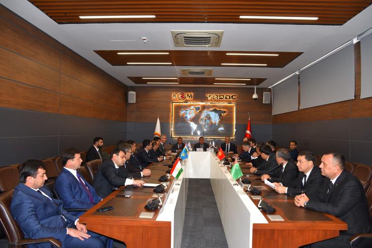 People in suits sit around a long conference table in a meeting room with flags on the table.