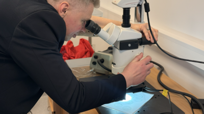 A person in a suit examines a sample under a microscope in a lab setting.