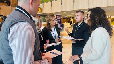 A small group of aviation security professionals stand in discussion inside Chișinău International Airport during an OSCE–ICAO training activity. Participants wearing accreditation badges review documents and exchange ideas in a bright airport terminal, reflecting the practical and collaborative nature of the Aviation Security (AVSEC) National Inspectors Course in Moldova.