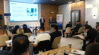 People attending a conference in a meeting room with a presentation on a screen.