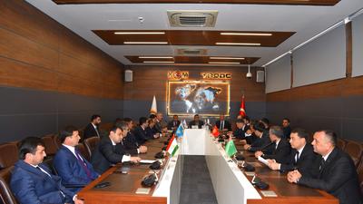 People in suits sit around a long conference table in a meeting room with flags on the table.